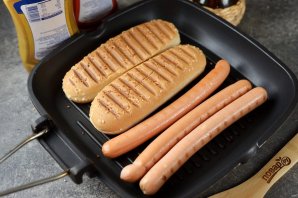 Хот-дог с жареным луком и солёными огурцами на сковороде Хот-дог с жареным луком и солёными огурцами на сковороде